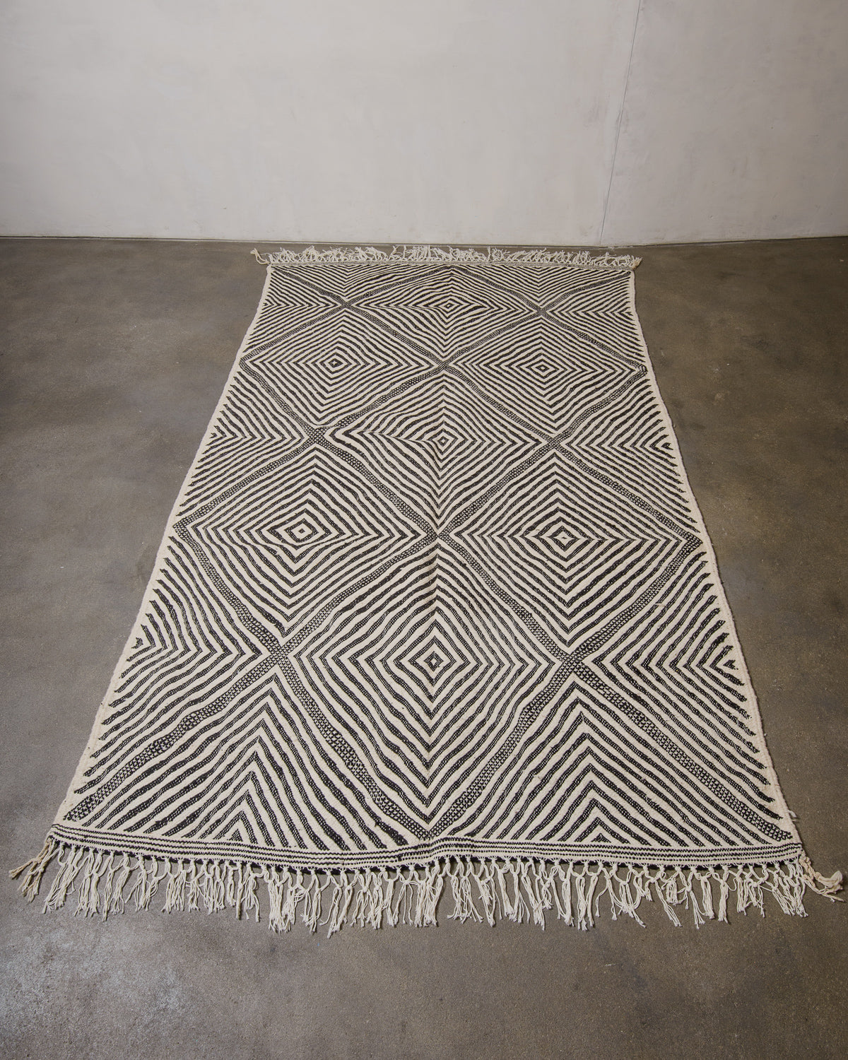 Woven Berberlin Kelim rug with geometric pattern on a concrete floor.